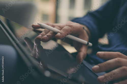 Closeup view of male hands holding stylus pen and working on a digital tablet. Blurred background. Horizontal.