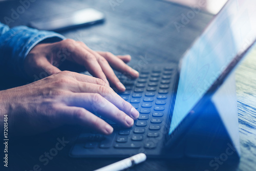 Closeup view of male hands typing on electronic tablet keyboard-dock station. Businessman working at office while sitting at wooden table.Horizontal,cropped.