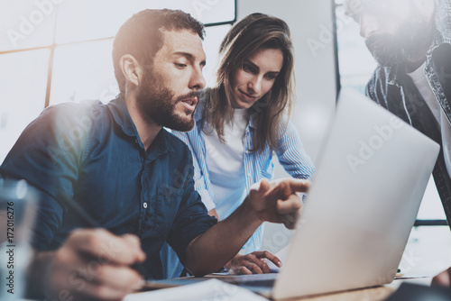 Group of coworkers sitting at the wooden table and working together on new startup project in modern loft office.Horizontal.Blurred background. photo