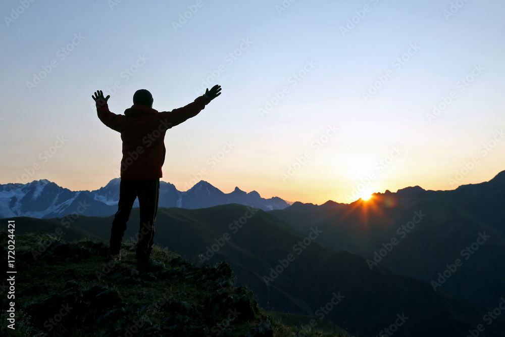 man with raised hands standing on the mountain face to sunrise.