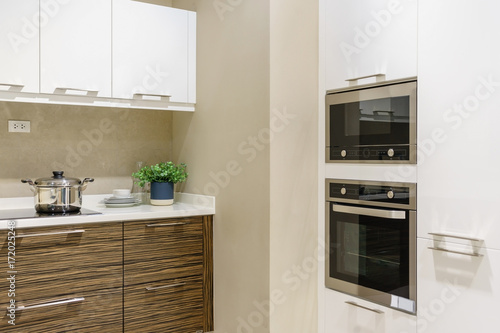 Modern kitchen furniture with contemporary kitchenware like hood, black induction stove, faucet and sink in house.