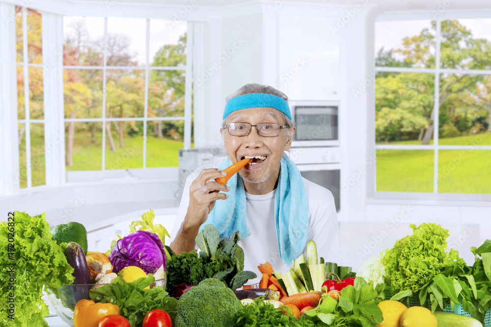 Old man biting carrot in the kitchen Old man biting carrot in the kitchen