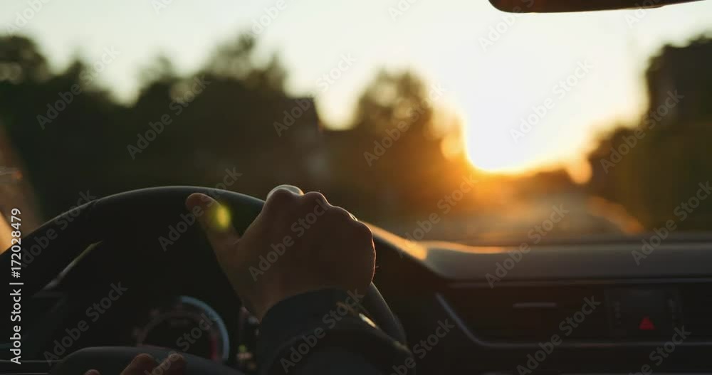 Man Driving a Car at Sunset. SLOW MOTION 4K DCi. Male Hand on steering wheel close up. Beautiful Road in blurred background.