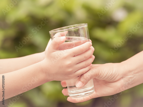 Closeup vintage woman hand giving glass of fresh water to child in the park.  Drink and health care concept.