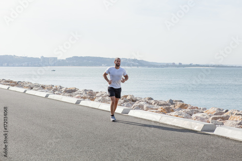 Serious Sporty Young Man Running on Seaside Road photo