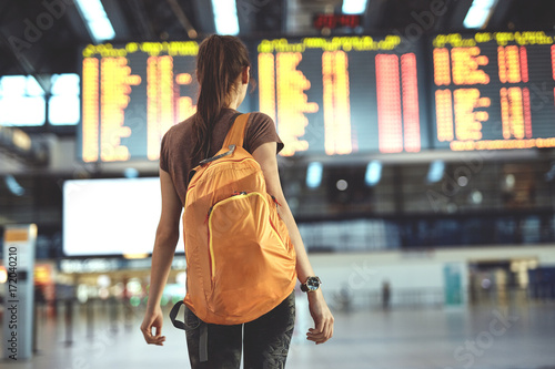 Young woman with small backpack as a hand luggage in international airport looking at the flight information board, checking her flight photo