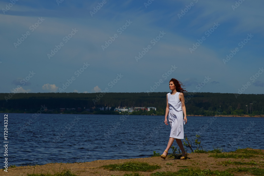 Beautiful woman in white dress walking near the river bank Beautiful woman in white dress walking near the river bank