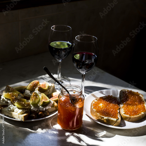 two glasses of red wine with sandwiches with red caviar and bruschettes with cheese and figs. in the kitchen at the window