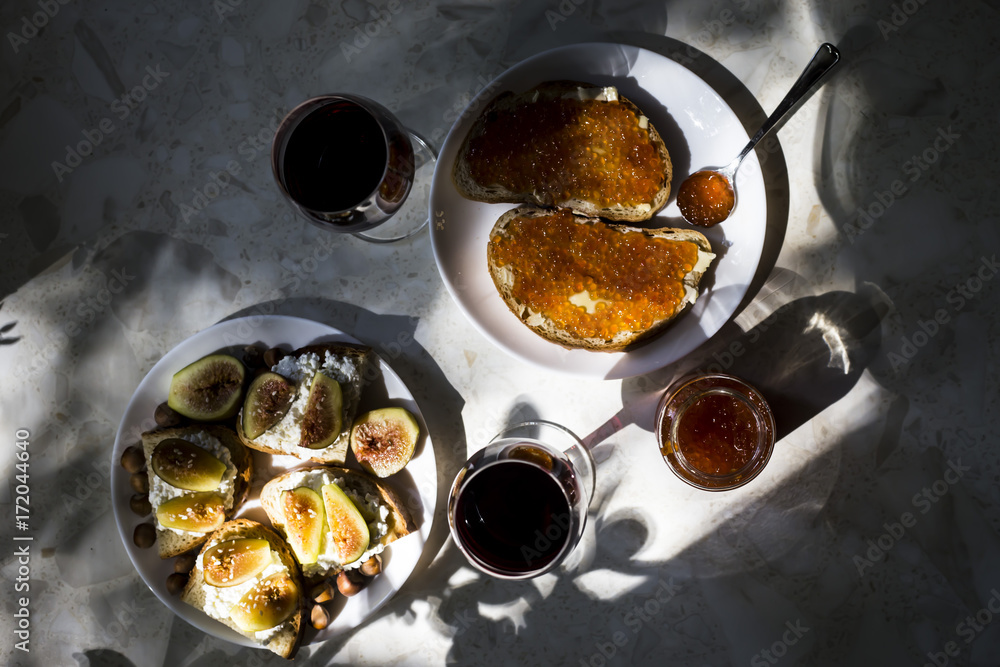 two glasses of red wine with sandwiches with red caviar and bruschettes with cheese and figs. in the kitchen two glasses of red wine with sandwiches with red caviar and bruschettes with cheese and figs. in the kitchen