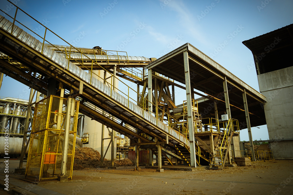 Particle board factory view of conveyor, lighting pole, building, logs storage Particle board factory view of conveyor, lighting pole, building, logs storage