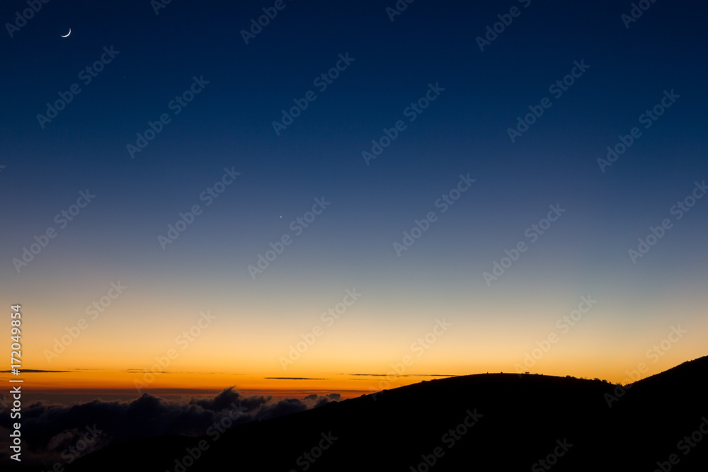 Mondsichel über dem vom Sonnenuntergang erleuchteten Horizont am Mauna Kea auf Big Island, Hawaii, USA.