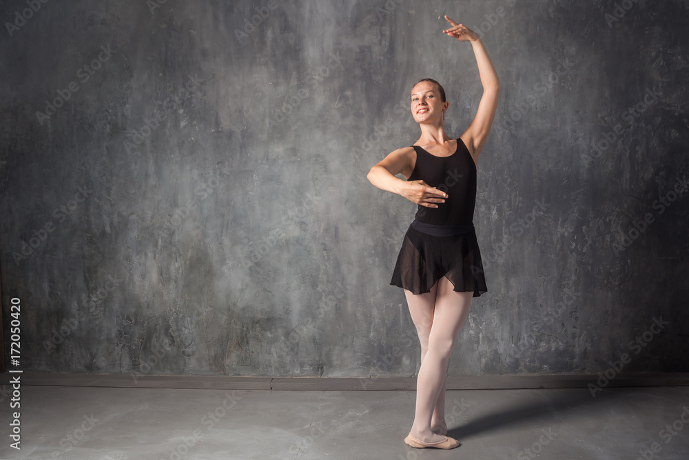beautiful young blonde ballet dancer in a black dress, white pantyhose and  bouillant pointes dancing Russian ballet in a dark dance studio Stock Photo