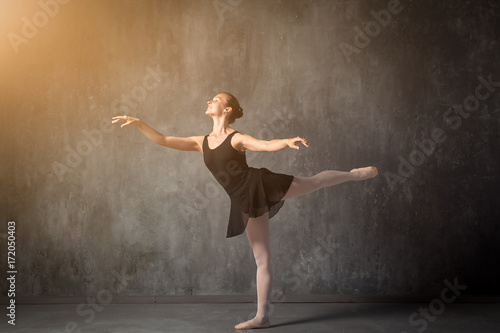 beautiful young blonde ballet dancer in a black dress, white pantyhose and bouillant pointes dancing Russian ballet in a dark dance studio photo