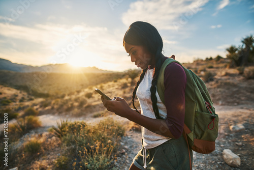 athletic african american woman with backpack looking at smart phone while hiking in red rock canyon nevada photo