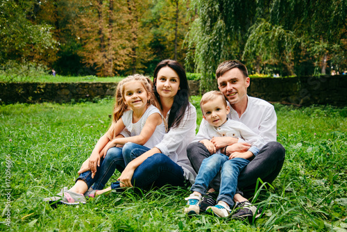 portrait of happy family mother, father, duaghter and son sit on the ground