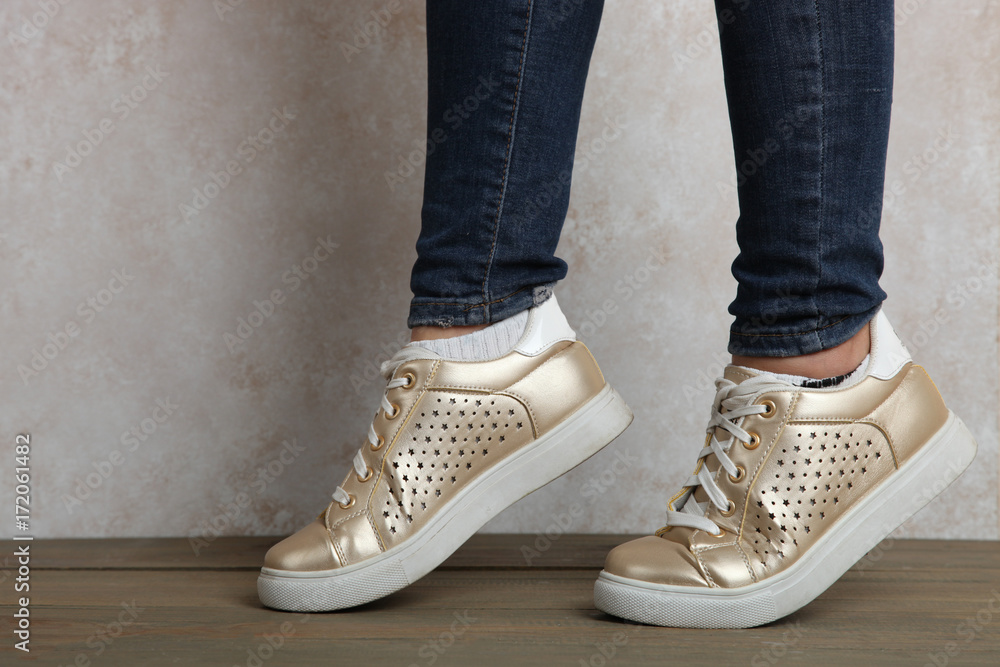 Female legs in gold sneakers Female legs in gold sneakers