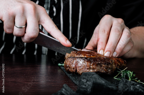 Hands cutting steak on plate with salad on dark background