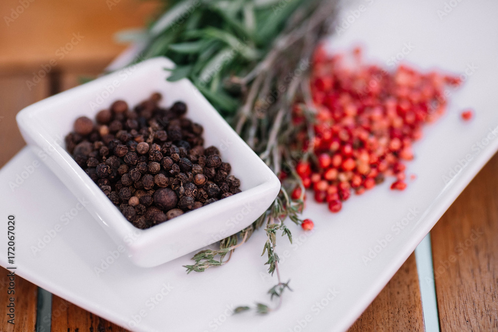 Rosemary with black and pink pepper corns on a white plate on wood background Rosemary with black and pink pepper corns on a white plate on wood background