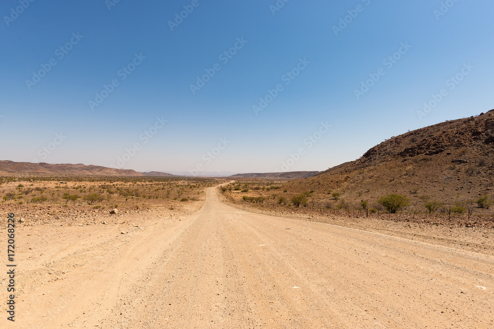 Gravel 4x4 road crossing the colorful desert at Twyfelfontein, in the majestic Damaraland Brandberg, scenic travel destination in Namibia, Africa. Gravel 4x4 road crossing the colorful desert at Twyfelfontein, in the majestic Damaraland Brandberg, scenic travel destination in Namibia, Africa.