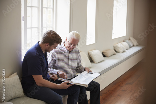 Fotografia Senior man sitting looking at photo album  with male nurse
