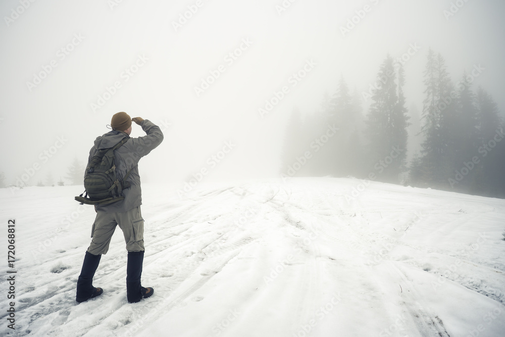 Man with backpack in the winter mountains peers into the foggy d