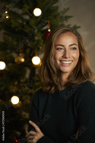 Stunning Christmas babe smiling by tree, looking away