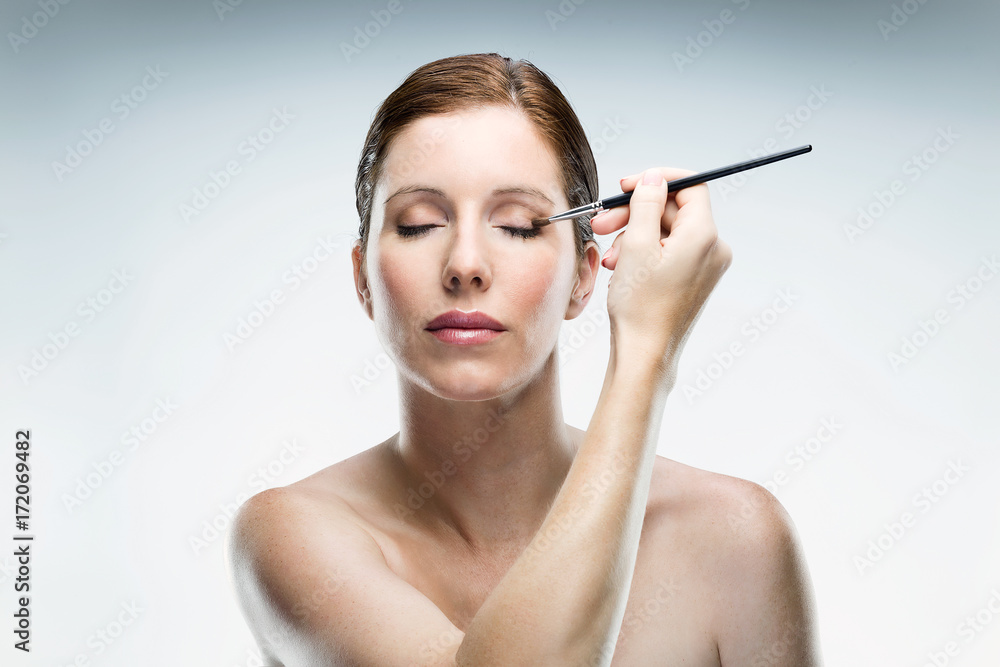 Beautiful young woman applying make up over white background. Beautiful young woman applying make up over white background.