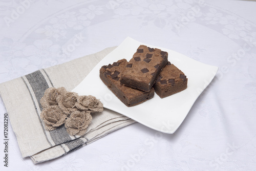 Chocolate brownie slices on a white plate with hessian flowers