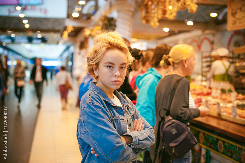 young beautiful woman in jeans clothes in business space of shopping center. portrait of a girl with freckles on her face, stylish girl standing near show-windows of fair in shopping center