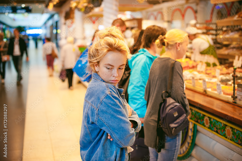 young beautiful woman in jeans clothes in business space of shopping center. portrait of a girl with freckles on her face, stylish girl standing near show-windows of fair in shopping center
