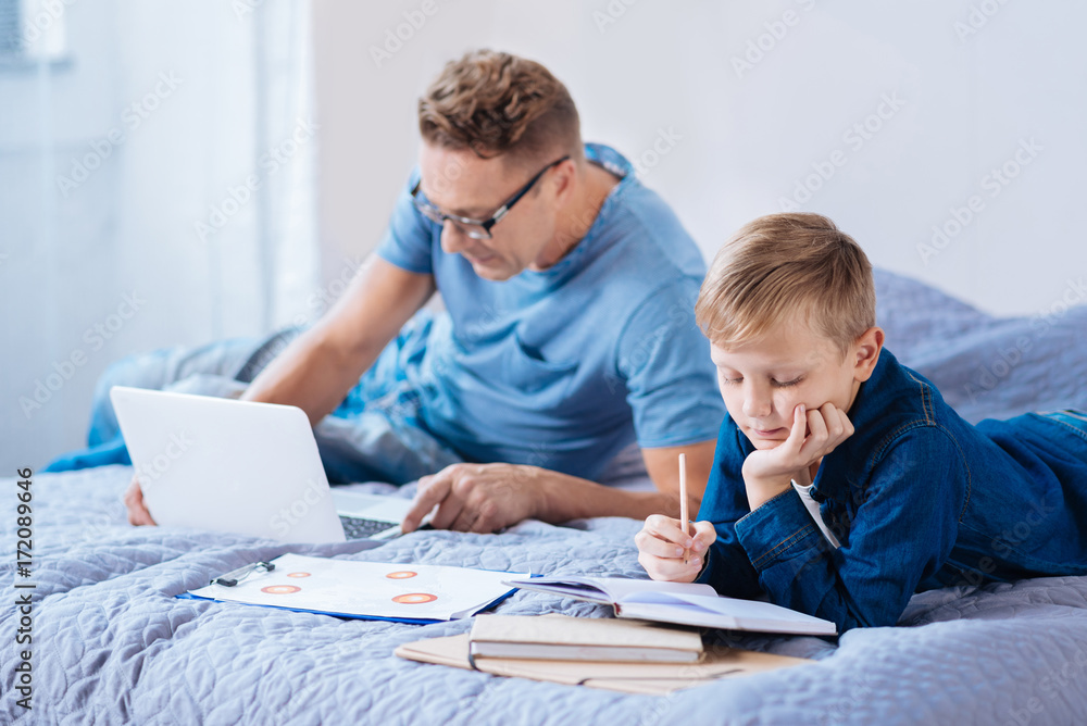 Little boy studying while his father working on laptop Little boy studying while his father working on laptop