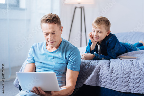 Little son watching his father work on laptop