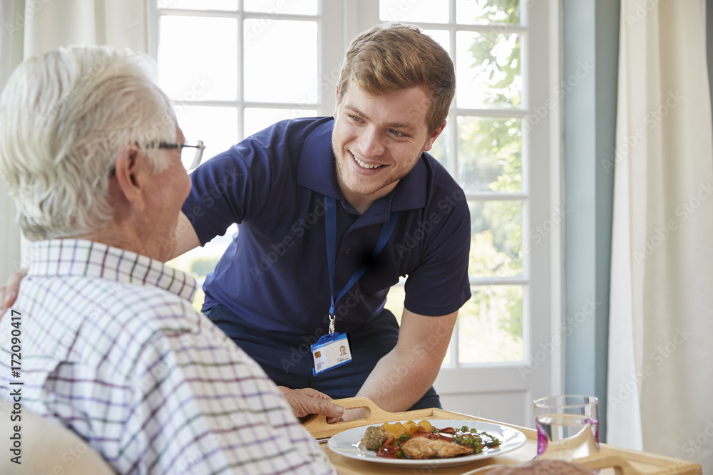 Male care worker serving dinner to a senior man at his home - obrazy, fototapety, plakaty 