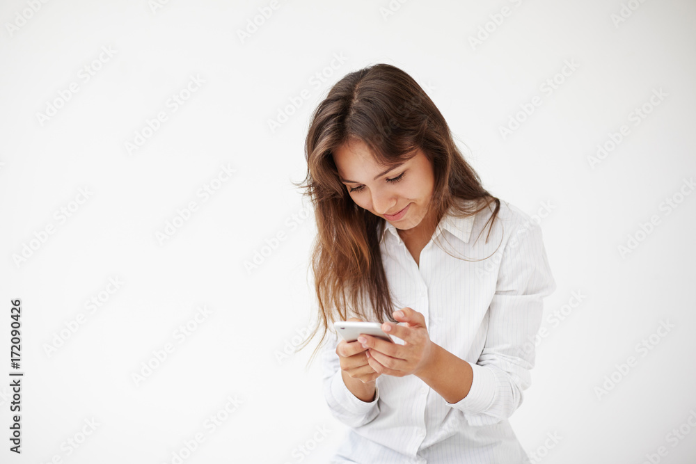 Always in touch. People, online communication and modern technologies. Attractive young brunette Hispanic woman manager with charming smile wearing white shirt using smart phone, typing text message Always in touch. People, online communication and modern technologies. Attractive young brunette Hispanic woman manager with charming smile wearing white shirt using smart phone, typing text message