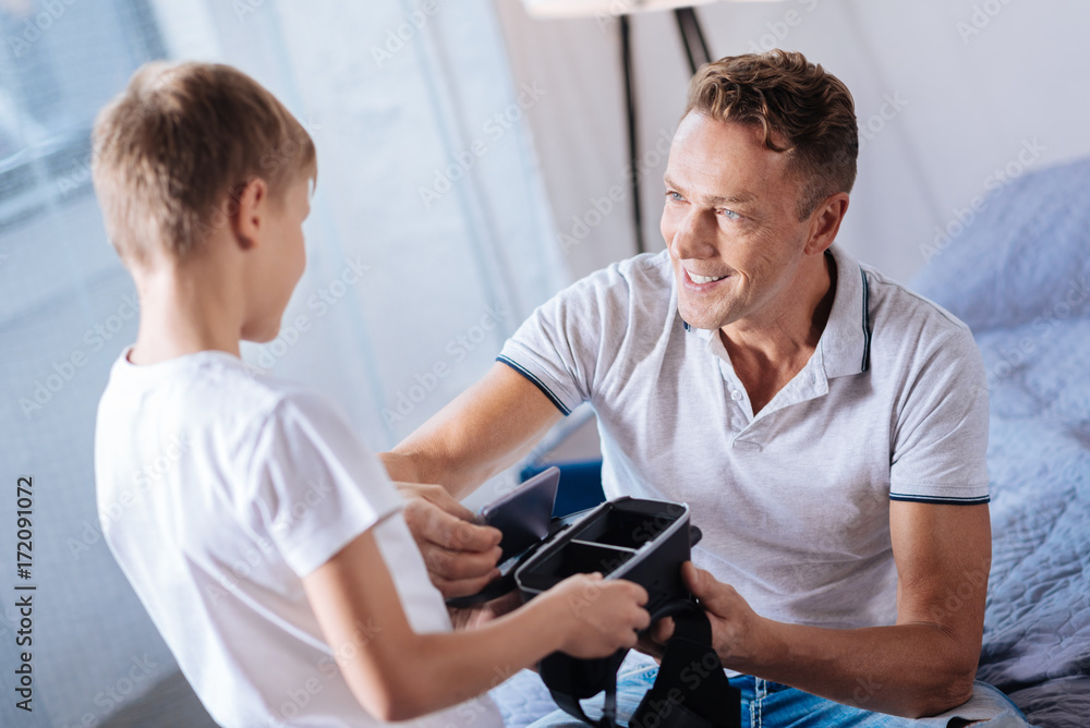 Smiling father inserting smartphone into sons VR headset Smiling father inserting smartphone into sons VR headset