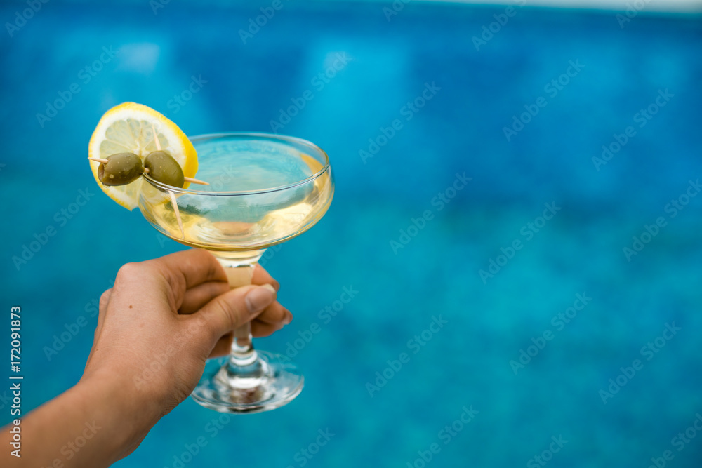 Fototapeta premium Bright martini cocktail on the pool background in hand