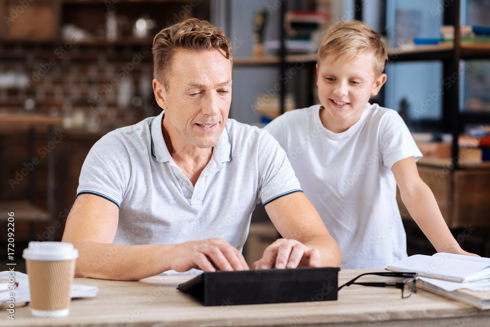 Smiling boy watching father type on tablet