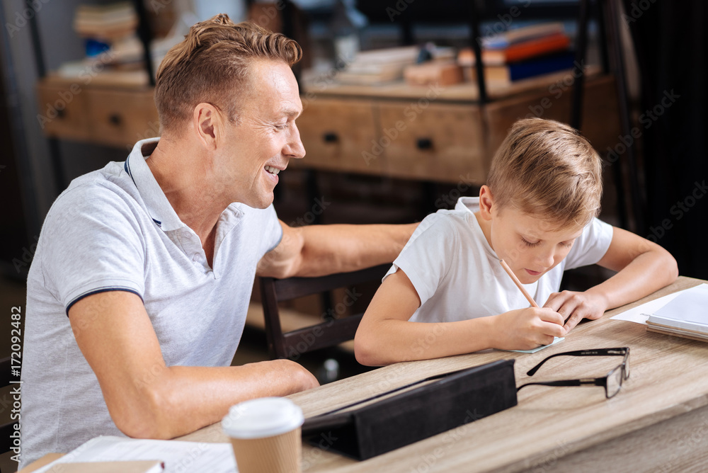 Smiling father watching his son write a note Smiling father watching his son write a note