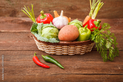 Fresh vegetables in a basket on a wooden background. Cabbage  bell pepper  potatoes  garlic  onion  chili and carrots. Harvest. Thanksgiving Day. Space for text.