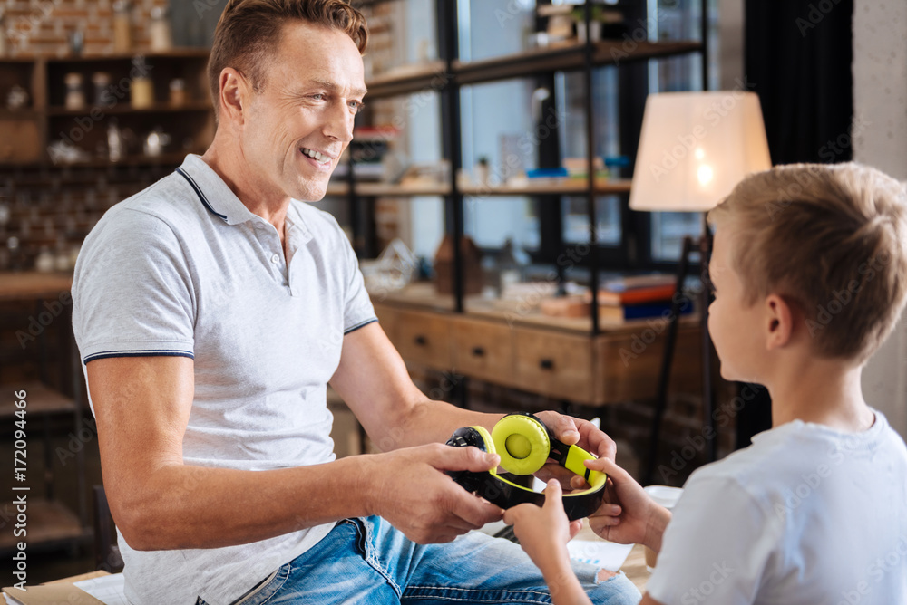 Fototapeta premium Smiling father taking headphones from his sons hands