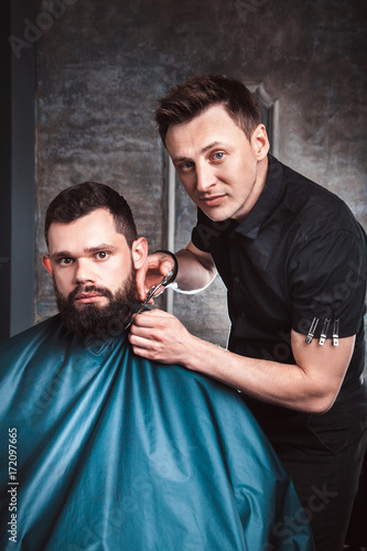 Handsome bearded man having his beard cut by hairdresser at the barbershop. A professional job with a dangerous razor, salon