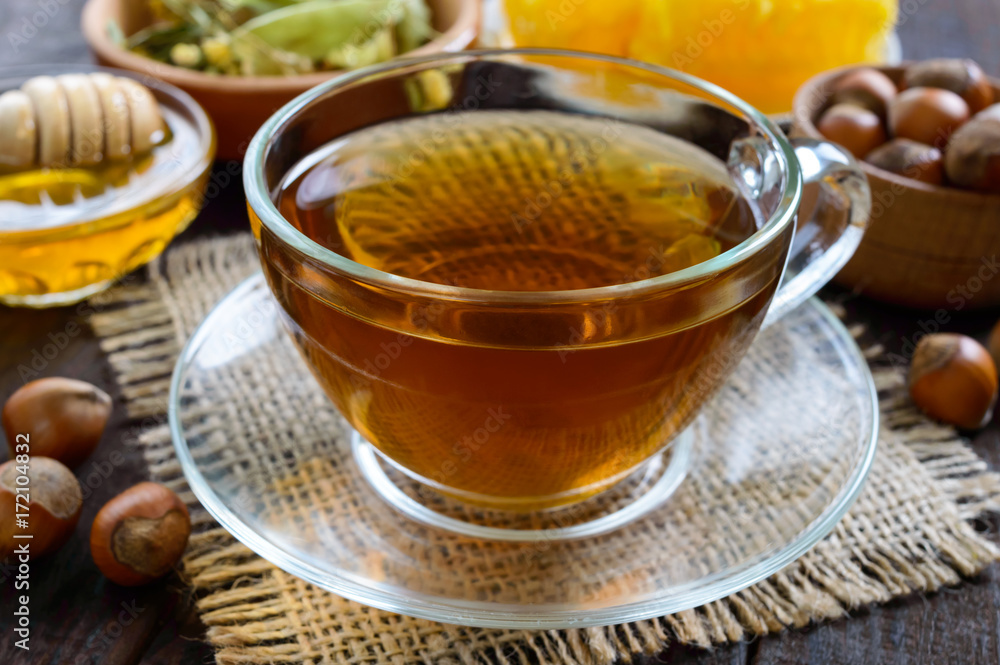 A cup of fresh fragrant herbal tea with honey and hazelnuts on a dark wooden background. Close-up. A cup of fresh fragrant herbal tea with honey and hazelnuts on a dark wooden background. Close-up.