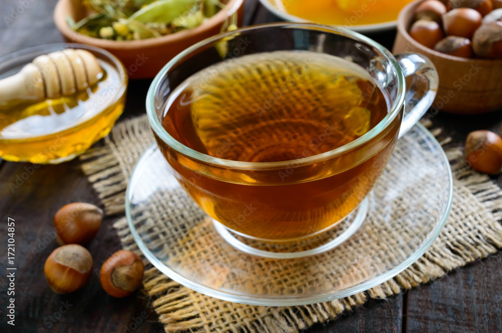 A cup of fresh fragrant herbal tea with honey and hazelnuts on a dark wooden background. Close-up. A cup of fresh fragrant herbal tea with honey and hazelnuts on a dark wooden background. Close-up.
