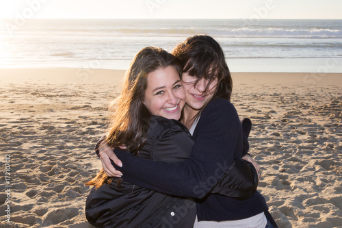 Mature mother with her teenage daughter looking in one direction on beach backlit with sun