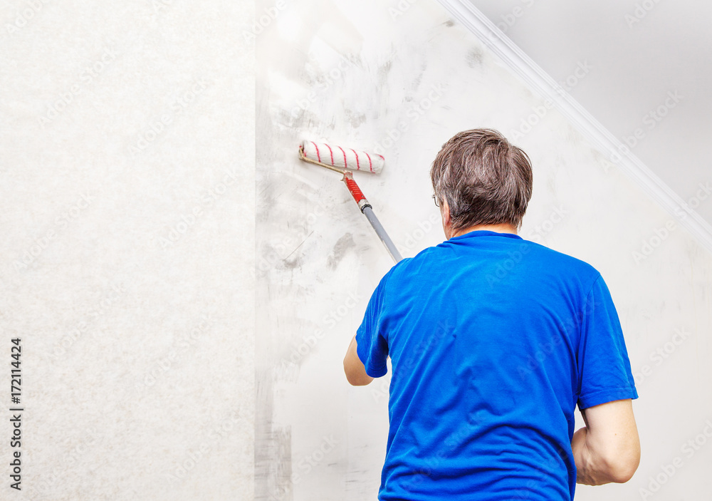 worker painting wall with background glue for a wallpaper worker painting wall with background glue for a wallpaper