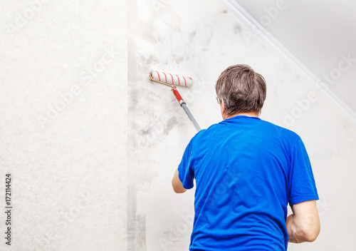 worker painting wall with background glue for a wallpaper