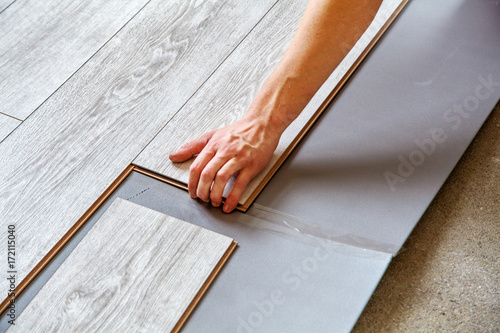 handyman's hands laying down laminate flooring boards