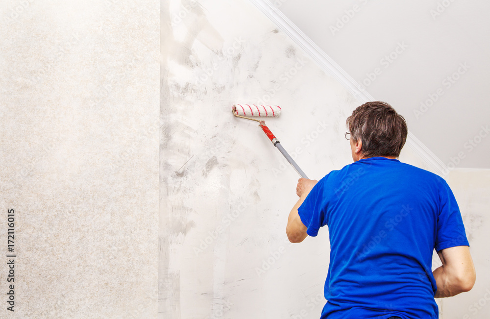 worker painting wall with background glue for a wallpaper worker painting wall with background glue for a wallpaper