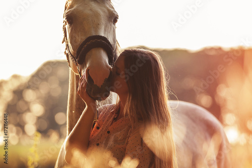 Woman kissing her horse at sunset, outdoors scene