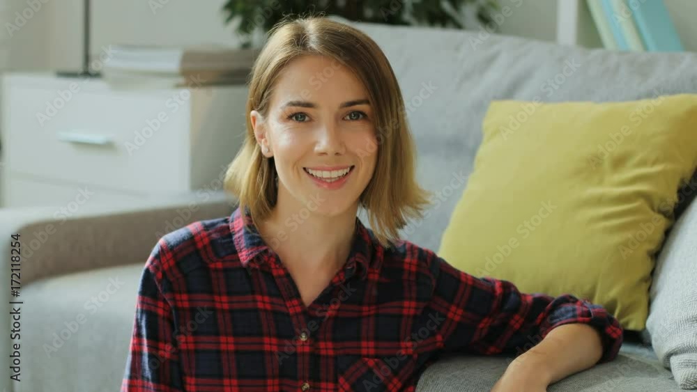 Portrait of young attractive woman smiling at the camera while sitting on the floor near sofa in the living room. Portrait of young attractive woman smiling at the camera while sitting on the floor near sofa in the living room.